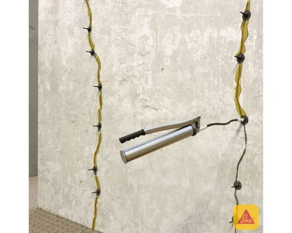 Grieta vertical en muro con líneas de inyección conectadas a pistola aplicadora de resina epóxica Sikadur 52