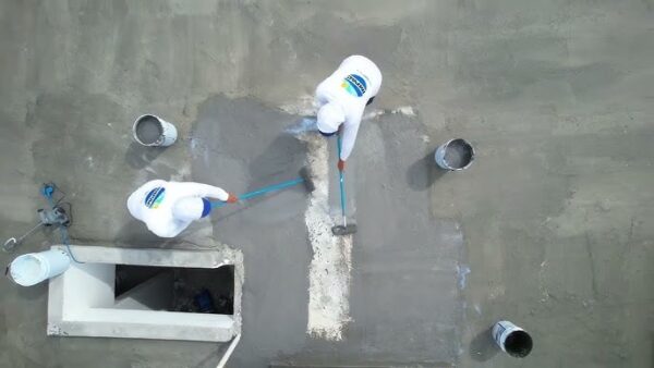 Dos aplicadores impermeabilizando superficie de cubierta con Impercrom Flex usando rodillos sobre estructura de concreto